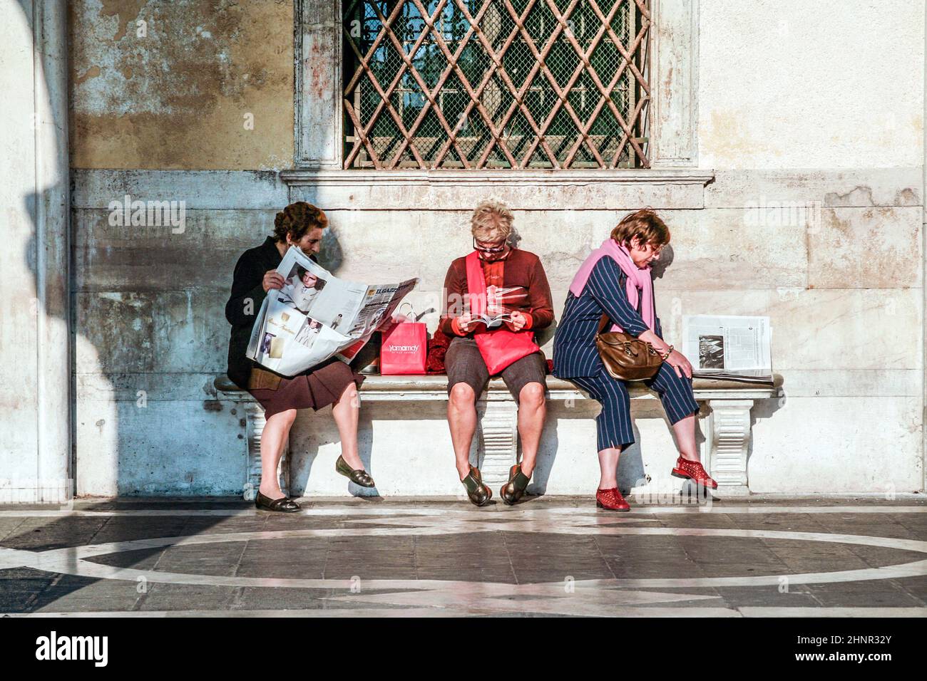 Frauen sitzen an einer Bank und lesen Zeitungen und Bücher Stockfoto