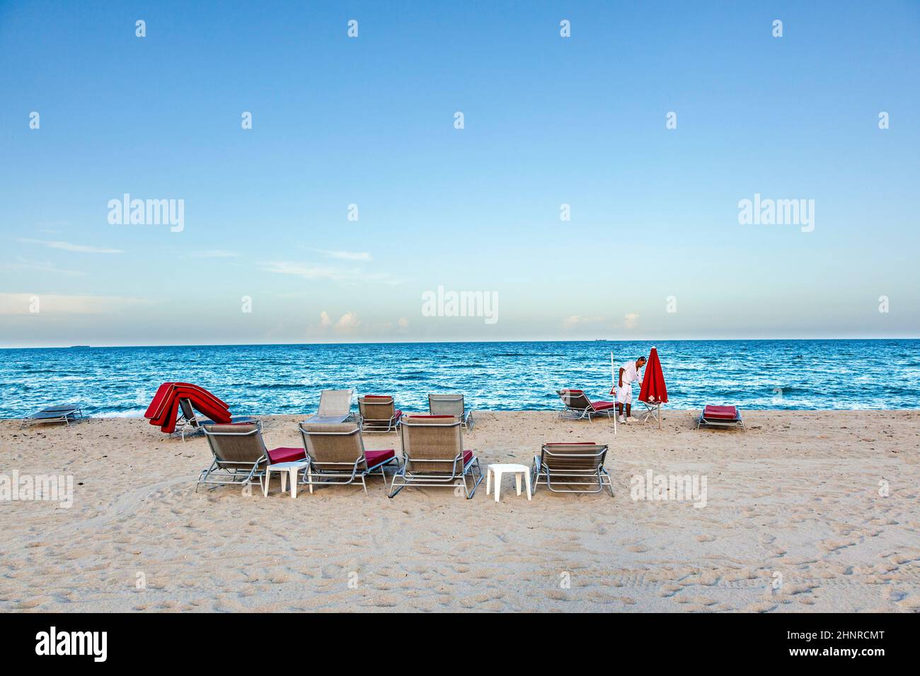 Der Hoteljunge sammelt am Ende des sonnigen Tages in Miami die roten Divan-Betten am South Beach ein Stockfoto