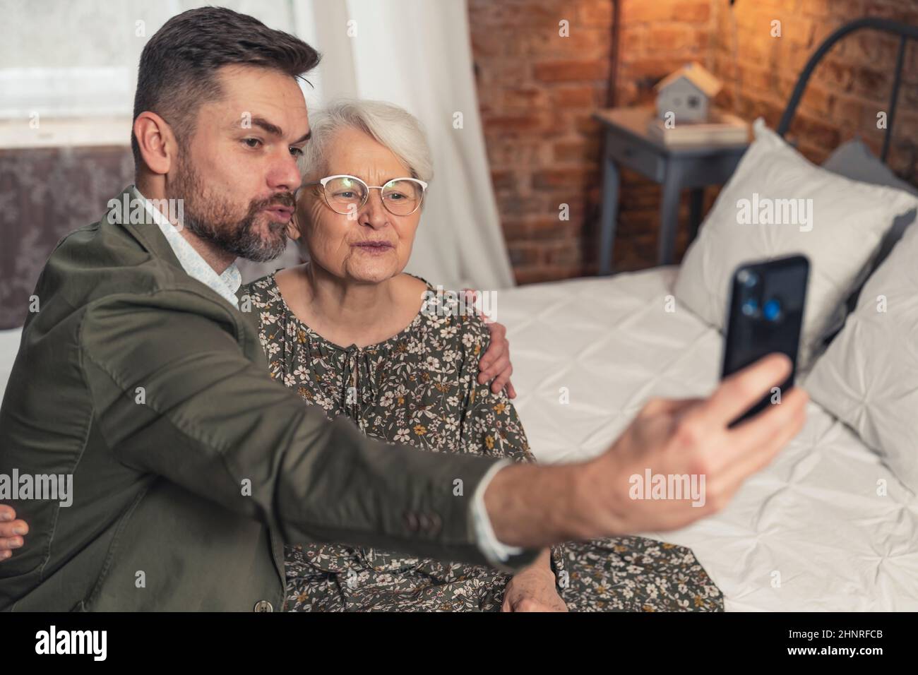 Die kurzhaarige Großmutter und ihr bärtiger Enkel machen Entengesicht und machen ein Selfie während des Großelterntags der Großmutter. Hochwertige Fotos Stockfoto