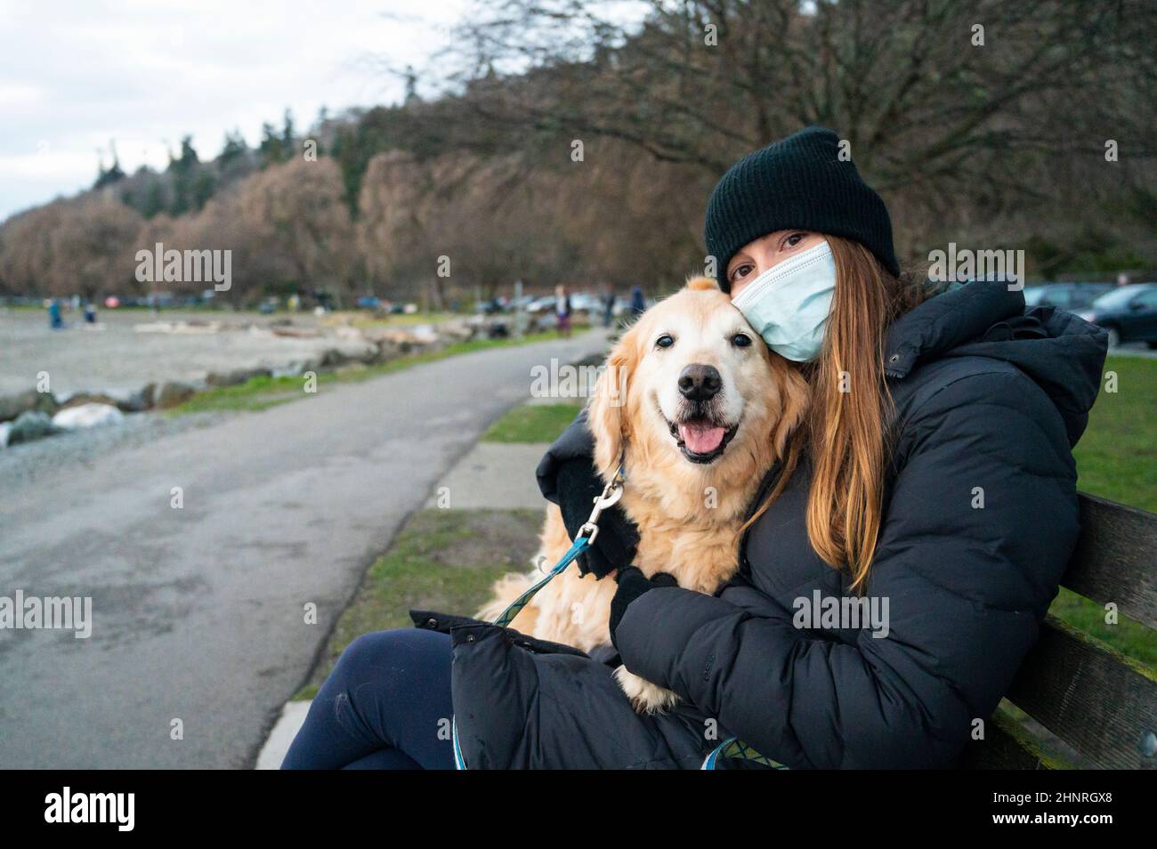 Hündin, die auf der Parkbank sitzt und ihren Hund in Maske trägt Stockfoto