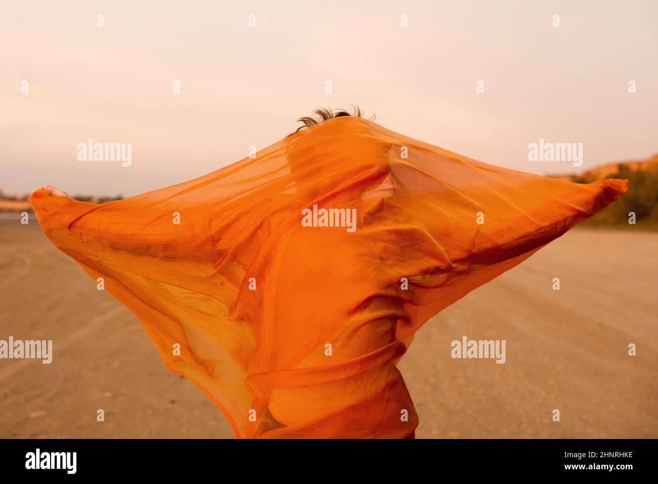 Frau mit orangefarbenem Tuch in der Wüste mit Wind Stockfoto