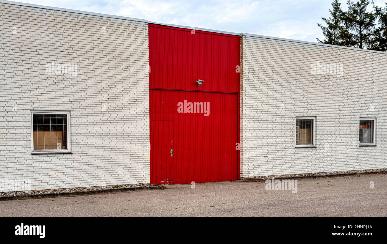 Rote Tür und Tor an einer weißen Backsteinmauer vor einem Lagerhaus mit Gitterfenstern, Frederikssund, Dänemark, Februar 17, 2022 Stockfoto