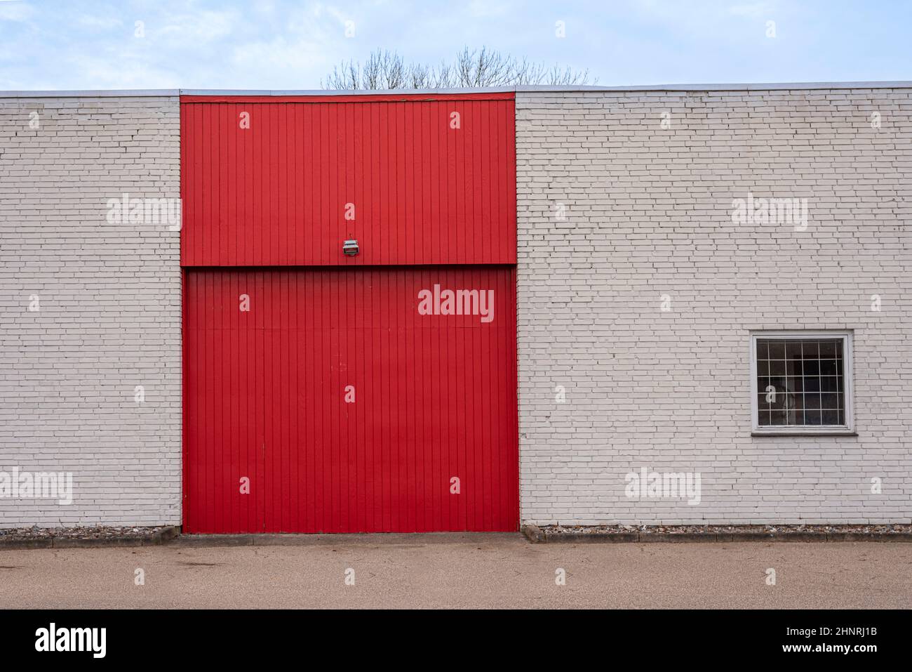 Rotes Tor an einer weißen Backsteinmauer vor einem Lagerhaus mit einem Fenster mit Gittern, Frederikssund, Dänemark, Februar 17, 2022 Stockfoto