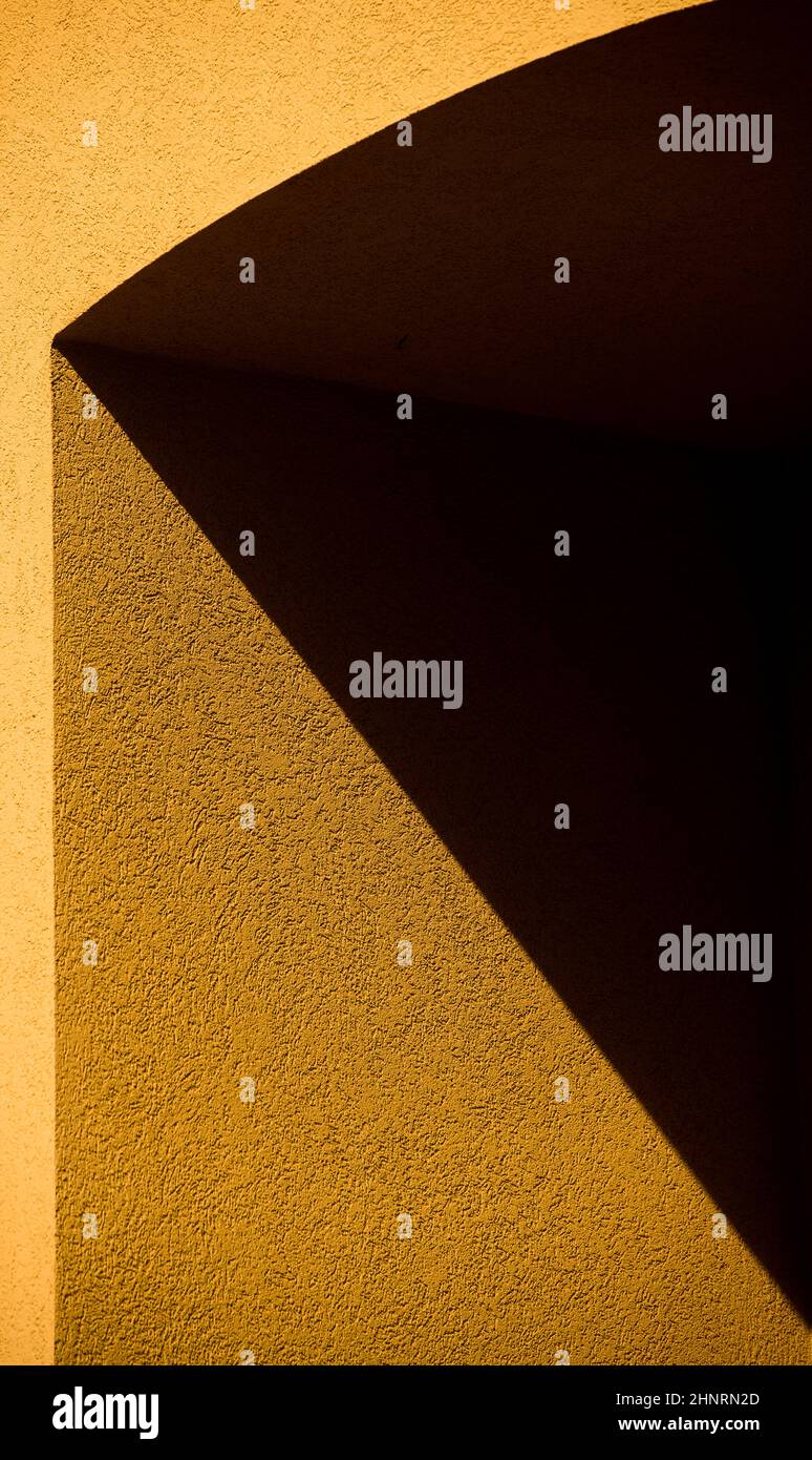 Geometrische Formen und Winkel von Schatten auf gelbe Außenzementbetonwand des Gebäudes oder Hauses in der Nachmittagssonne im Freien Dreiecksformen Stockfoto