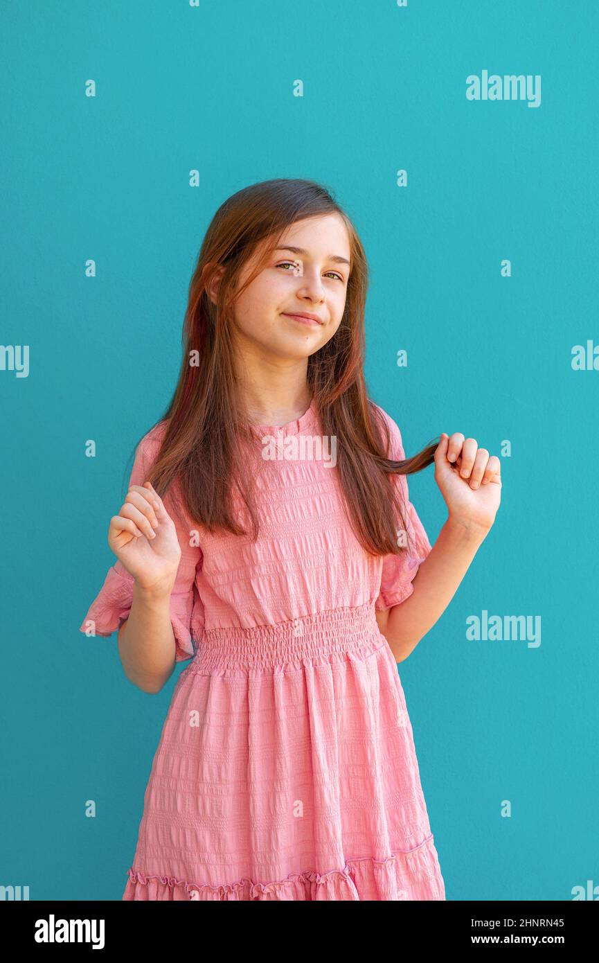 Porträt eines Teenagers Mädchen. Nettes Mädchen mit langen Haaren auf einem türkisfarbenen Hintergrund in einem rosa Kleid. Stockfoto