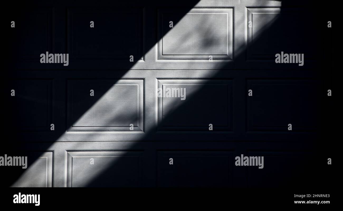 Abstraktes Schwarz-weiß-Design von Schatten und Quadraten auf weißem Garagentor des Hauses in urbaner Umgebung, Lichtstreifen zwischen zwei schwarzen Dreiecken Stockfoto