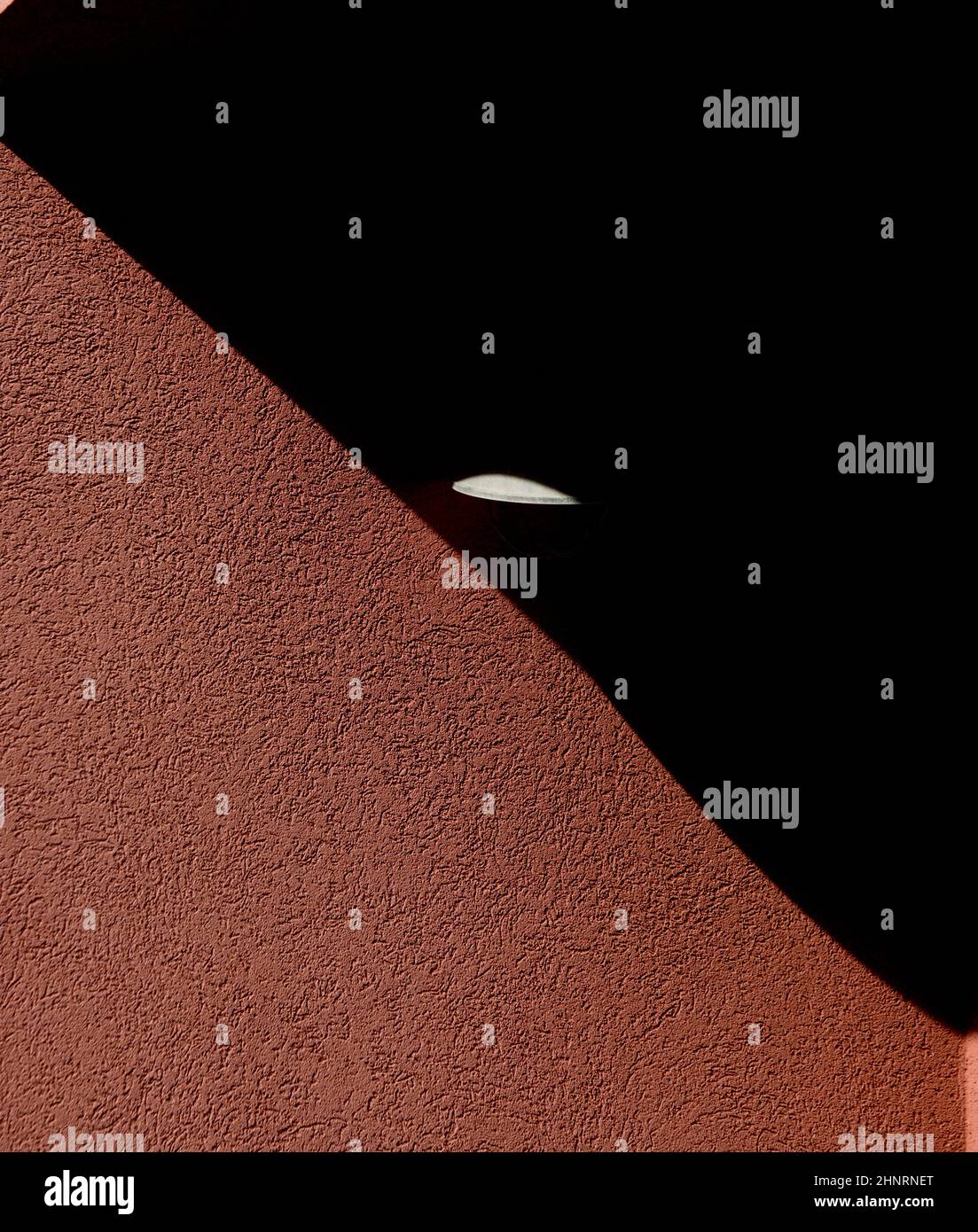Abstraktes Design von Schatten auf der Außenseite des Hauses oder Gebäudes strukturierter Beton- oder Zementwand mit winzigem Licht, das im dreieckigen Schatten ge leuchtet Stockfoto
