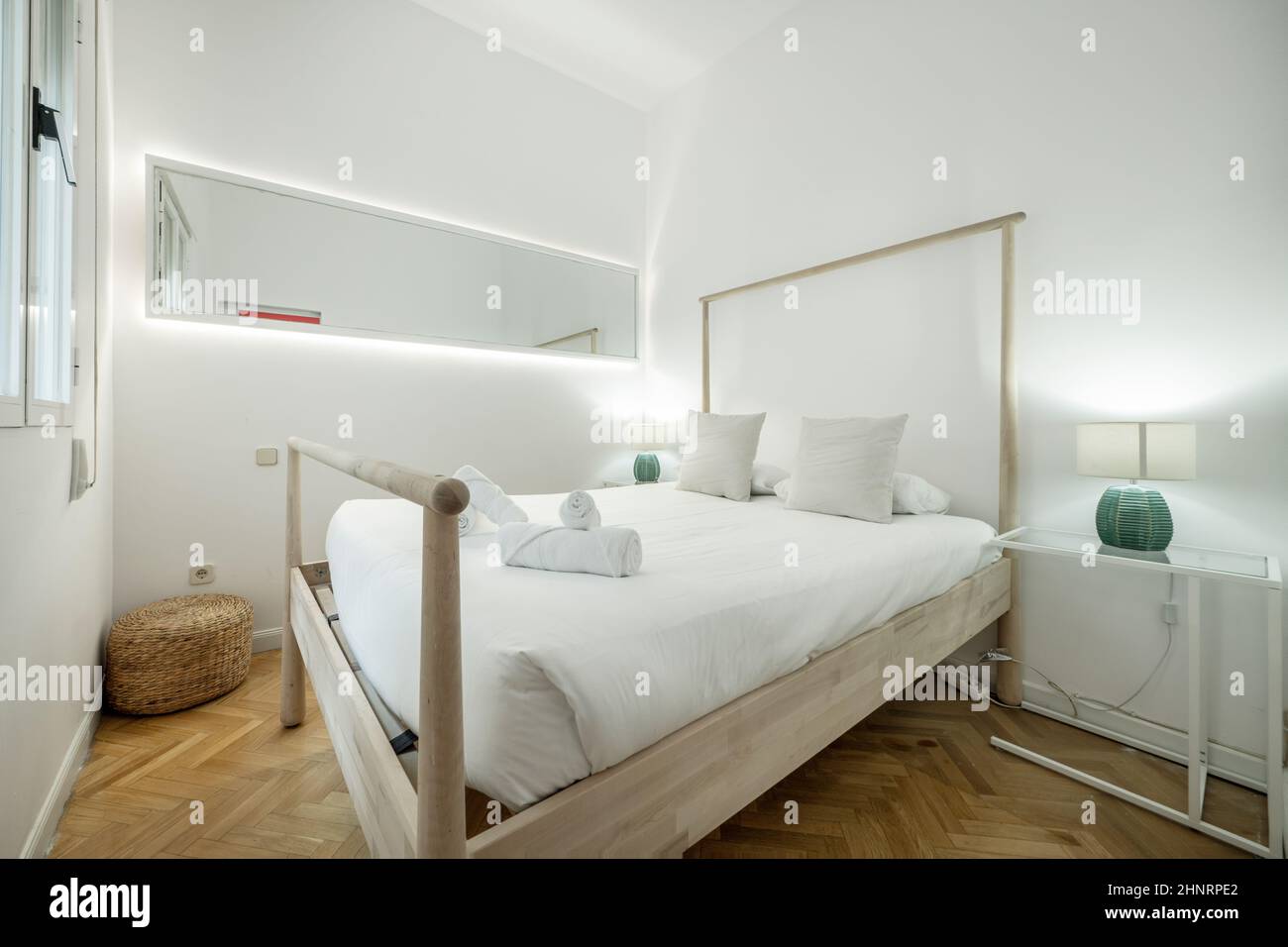 Schlafzimmer mit Holzbett mit Geländer, weißer Steppdecke, großem langen Spiegel und Lampen auf den Nachttischen Stockfoto