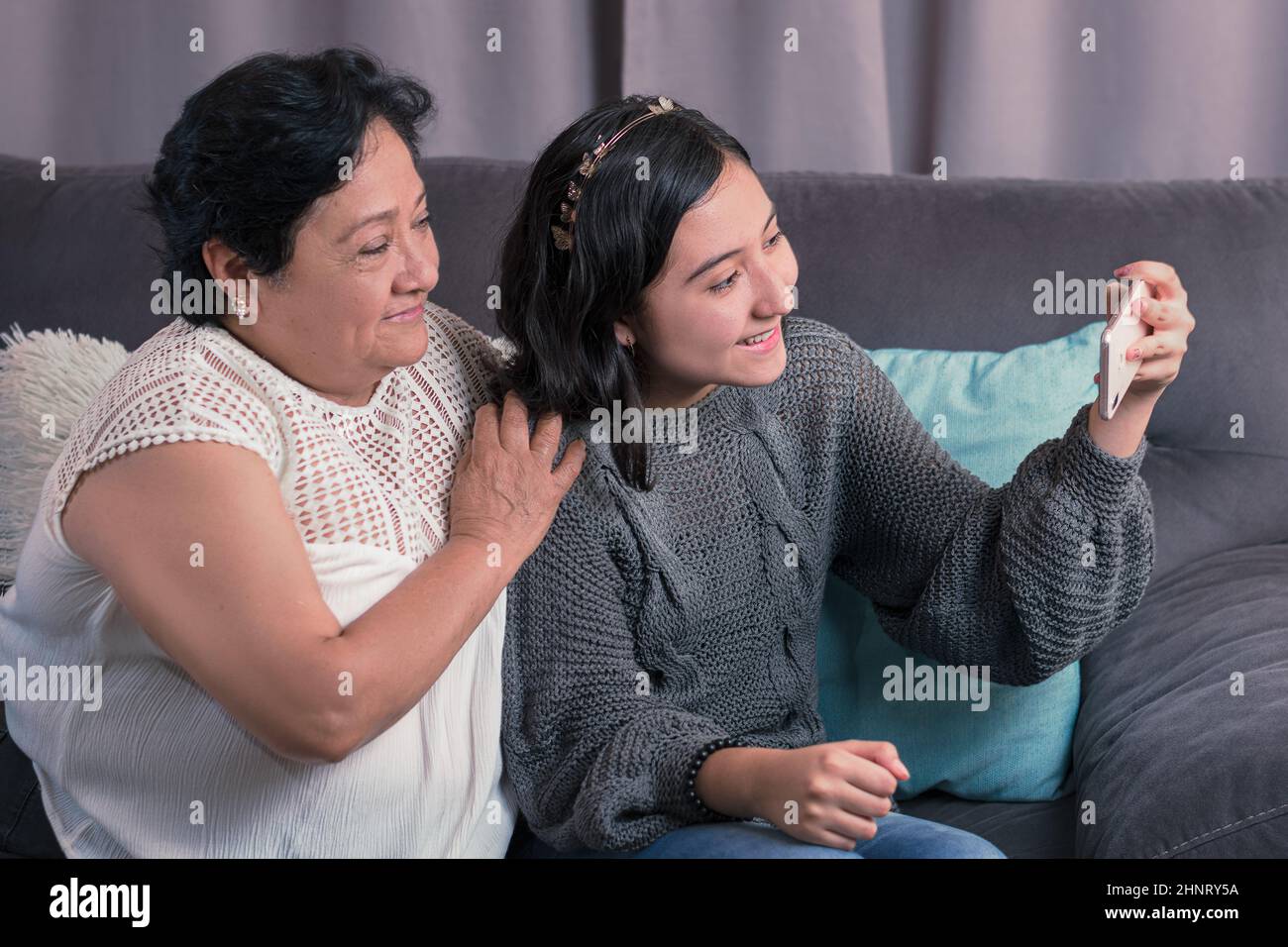 Ältere Frau 60 Jahre alte lateinische Großmutter mit Handy und Spaß mit ihrer Enkelin fotografieren und Videos ansehen Stockfoto