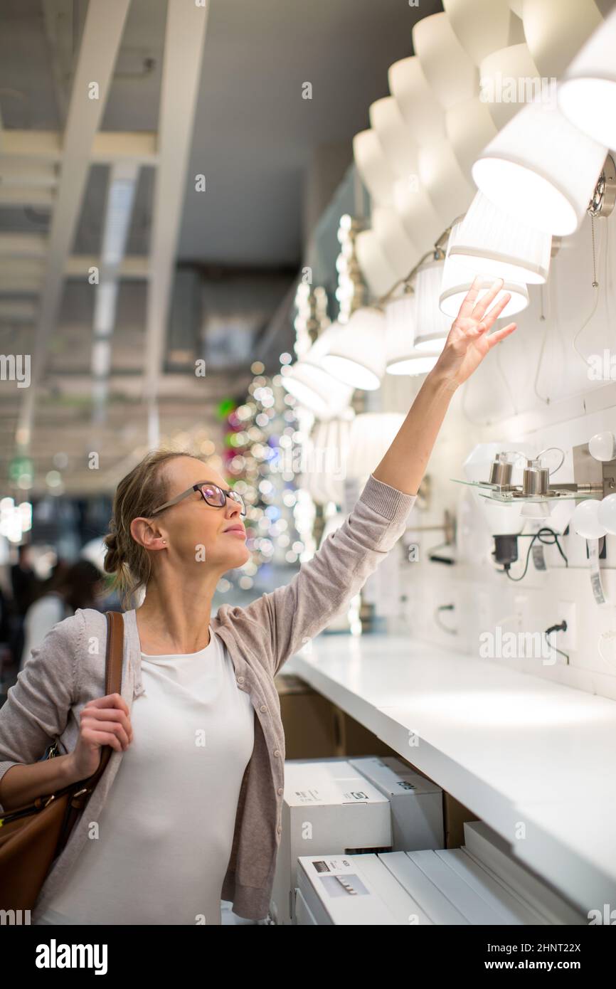 Hübsche, junge Frau das richtige Licht für Ihre Wohnung in einem modernen Home Furnishings Store (Farbe getonte Bild flach DOF) Stockfoto