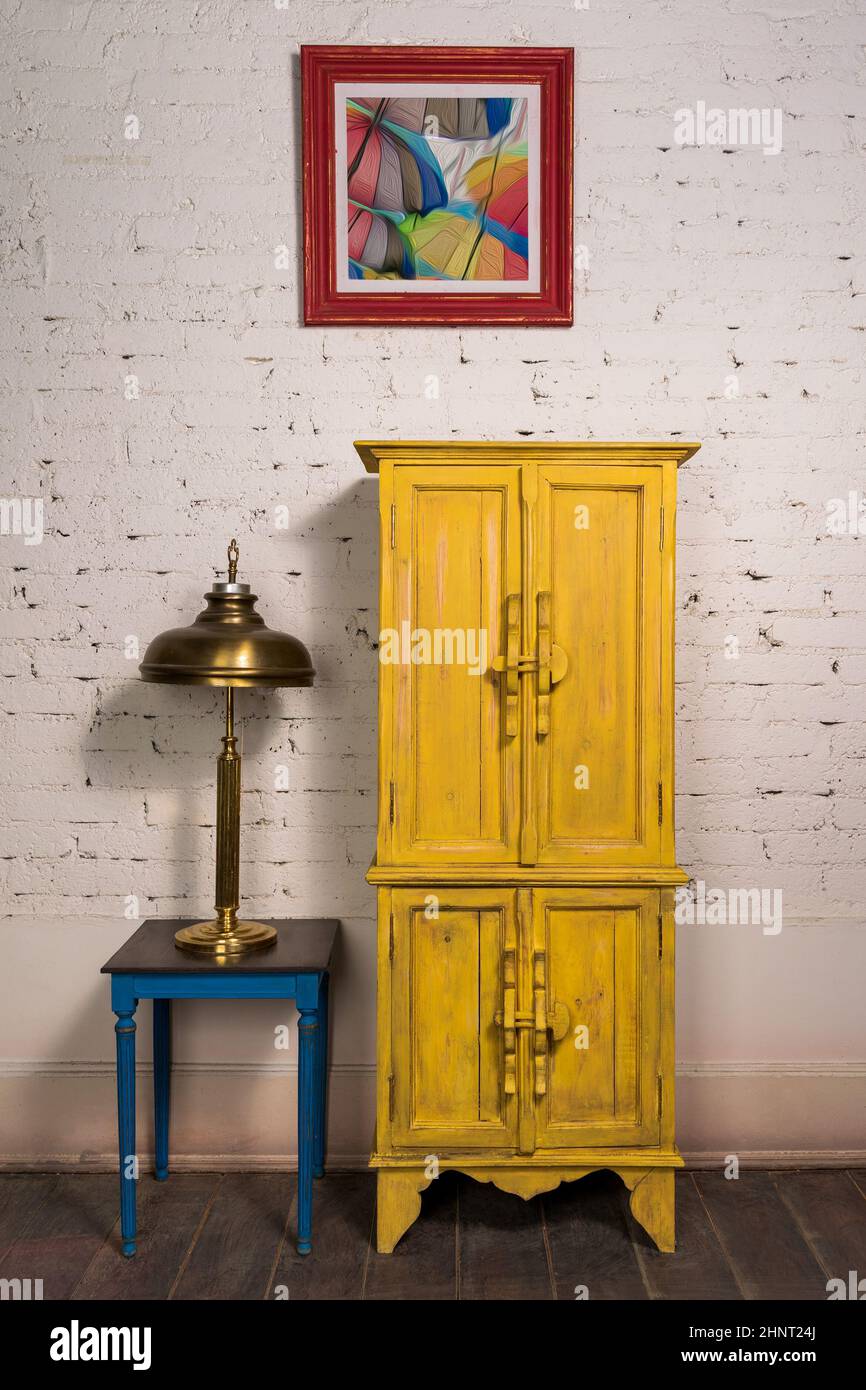 Vintage gelben Schrank, Malerei, Messing Tischlampe und Vintage-Tisch auf dunklem Holzparkett und weißen Ziegelwänden Stockfoto