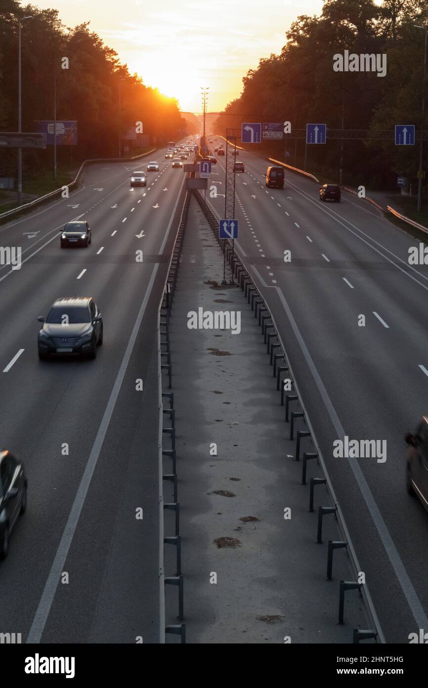 Autos auf der Autobahn bei Sonnenuntergang bewegen. Straßenverkehr bei Sonnenuntergang mit Autos. Viel Verkehr auf der Autobahn, Blick von oben auf die Straße. Stockfoto