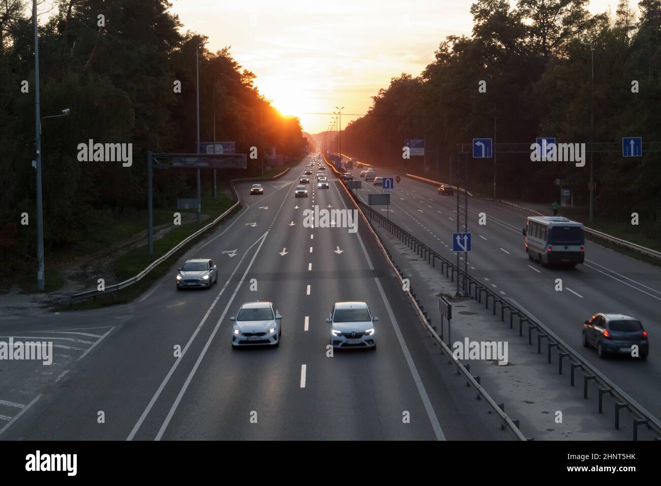 Autos auf der Autobahn bei Sonnenuntergang bewegen. Straßenverkehr bei Sonnenuntergang mit Autos. Viel Verkehr auf der Autobahn, Blick von oben auf die Straße. Stockfoto