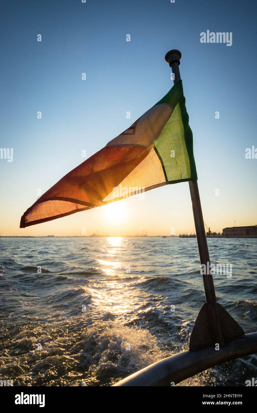 Bei Sonnenuntergang winkt die italienische Flagge auf dem Rücken eines Bootes in venedig Stockfoto