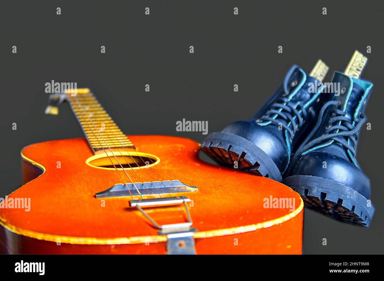 Rock und Roll Konzept. Schwarze Stiefel und akustischer Gitarre. Rock und Roll Stiefel auf rosa Hintergrund Stockfoto