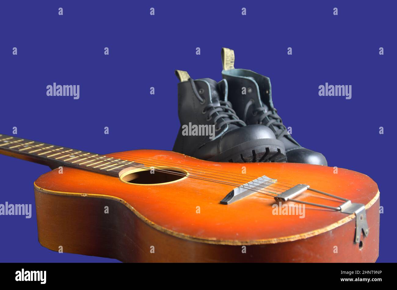 Rock und Roll Konzept. Schwarze Stiefel und akustischer Gitarre. Rock und Roll Stiefel auf marine blau hintergrund Stockfoto