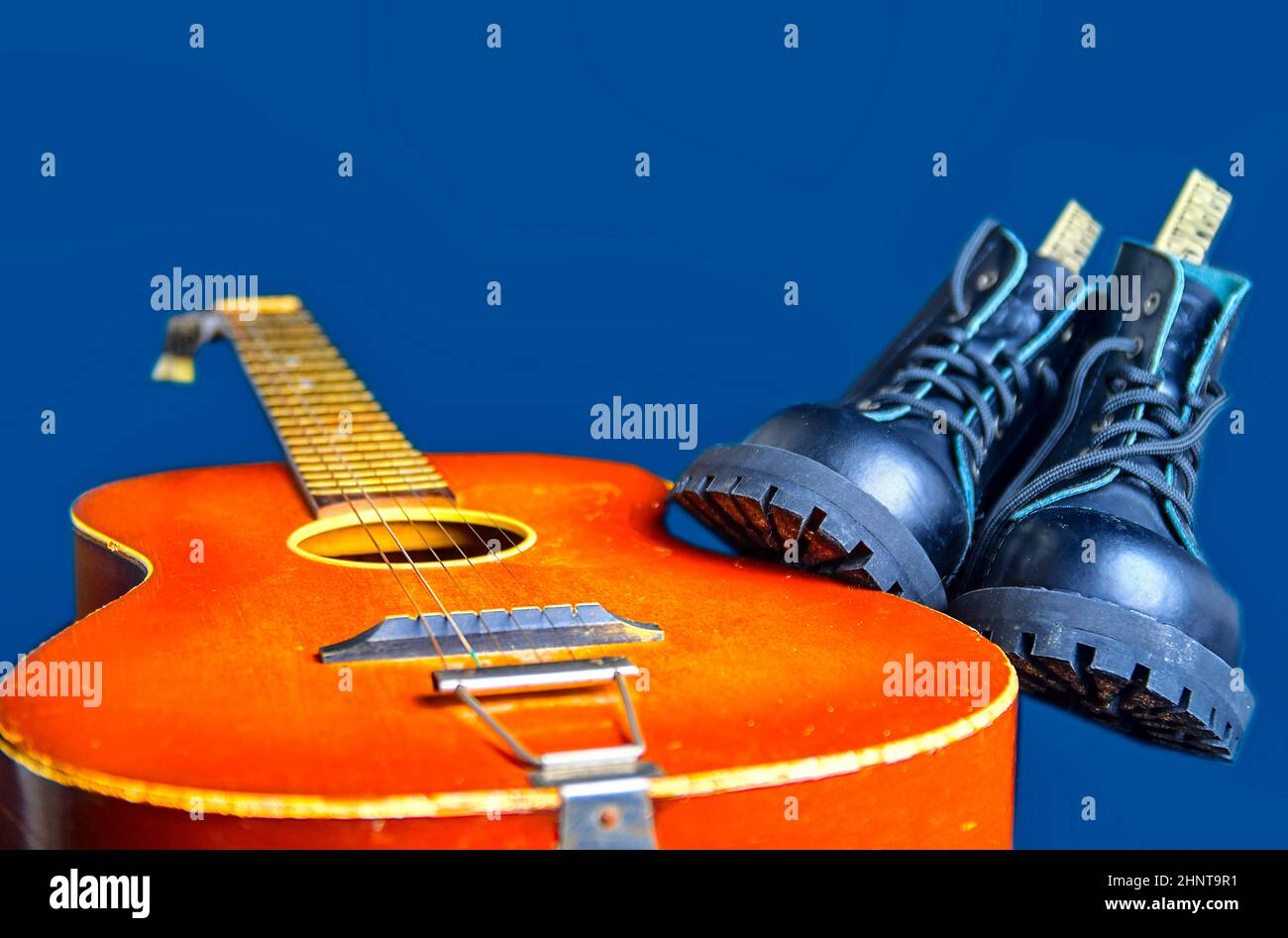 Rock und Roll Konzept. Schwarze Stiefel und akustischer Gitarre. Rock und Roll Stiefel auf marine blau hintergrund Stockfoto