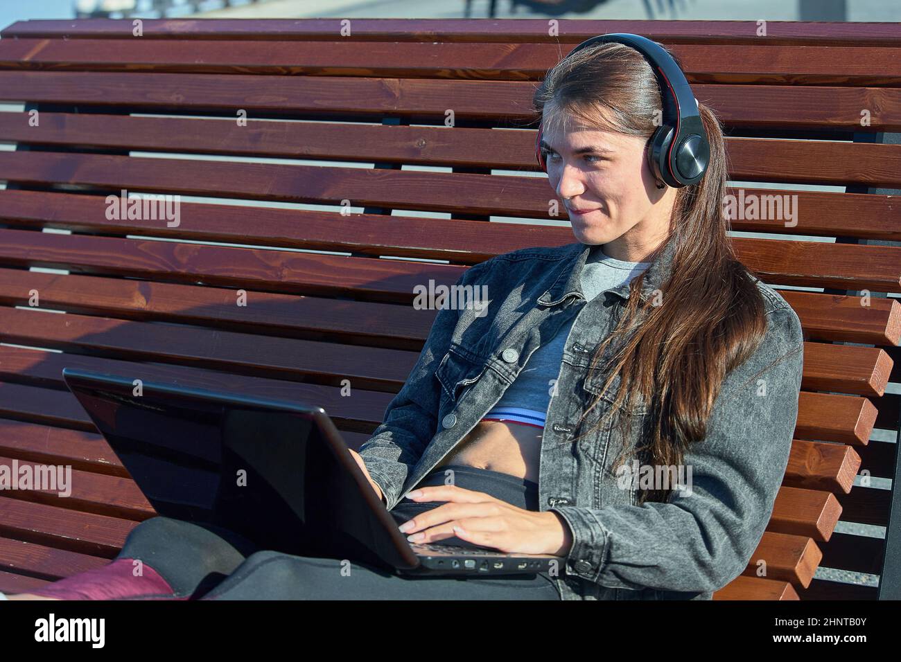 Eine Frau mit einem Laptop sitzt auf einer Außenbank und arbeitet online Stockfoto