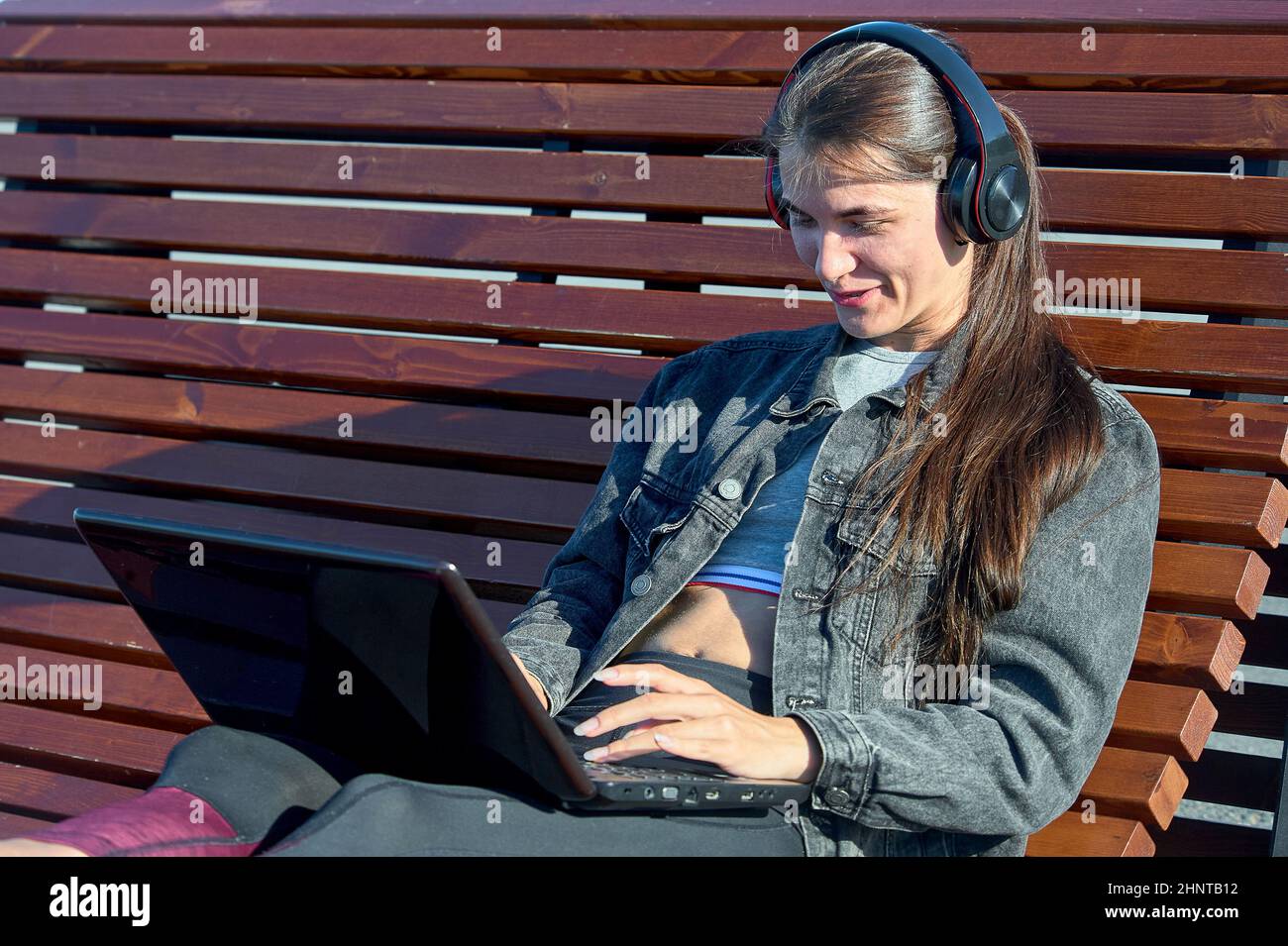 Eine Frau mit einem Laptop sitzt auf einer Außenbank und arbeitet online Stockfoto