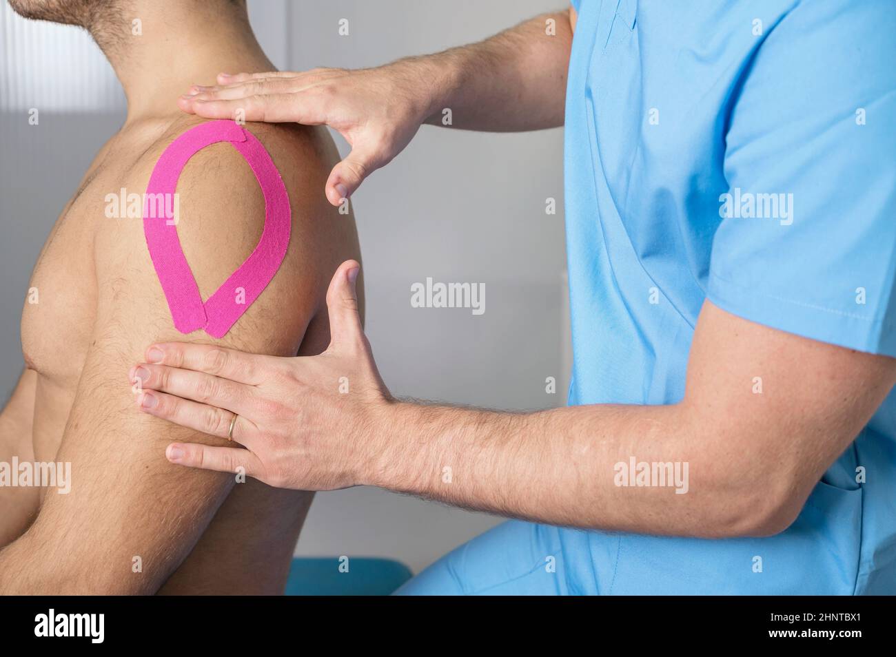 Physiotherapeut, der Kinesioband auf die Schulter des männlichen Patienten aufklebt. Kinesiologie, Physiotherapie, Rehabilitationskonzept. Nahaufnahme Stockfoto