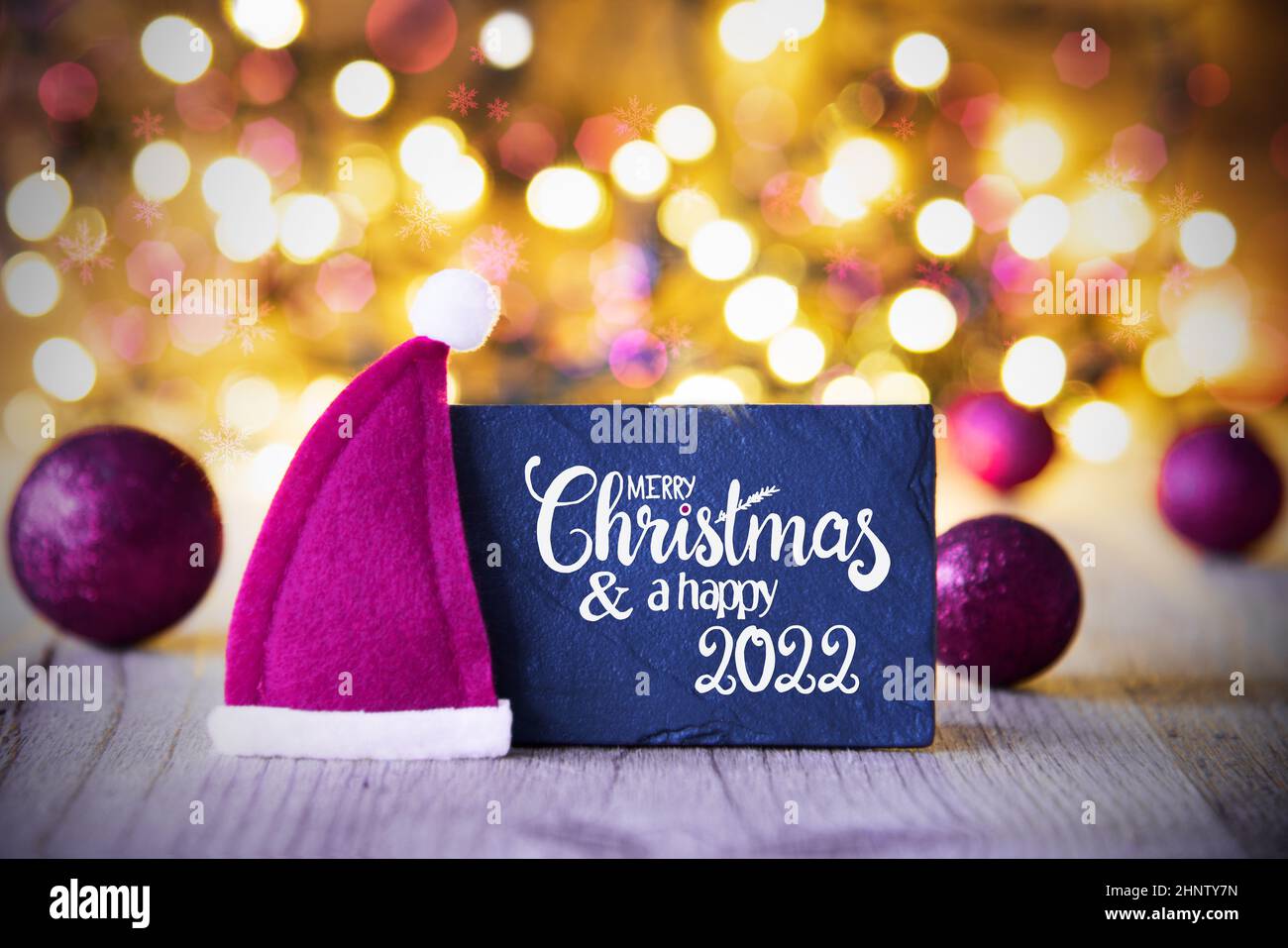 Sighn Wth Englisch Kalligraphie Frohe Weihnachten Und Happy 2022. Lila Weihnachtskugel Ornament Mit Weihnachtsmütze. Funkelnde Lichter Hintergrund Stockfoto