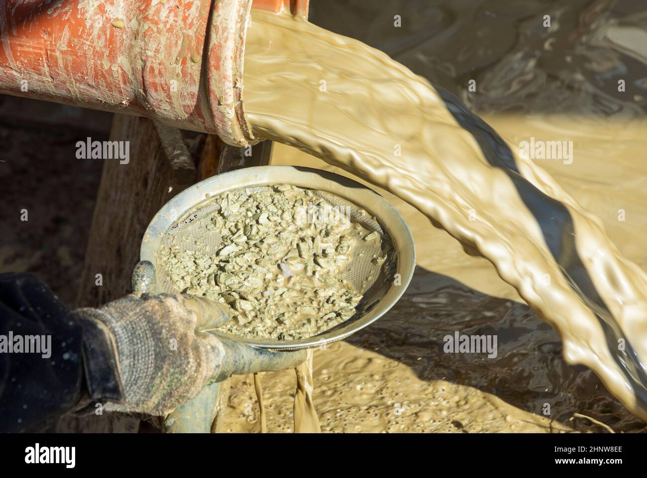 Wasser gemischt mit Lehm aus einer künstlichen Brunnenbohrmaschine und Steine von Hand mit einer Waschpfanne kontrolliert Stockfoto