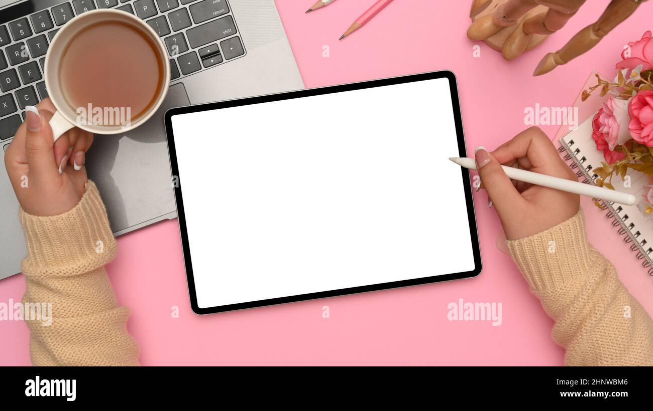 Beauty-Bloggerin Workspace, Eine Frau, die etwas auf ihrem digitalen Tablet skizziert, während sie an ihrem pinken Schreibtisch einen heißen Tee schlürft. Draufsicht Stockfoto