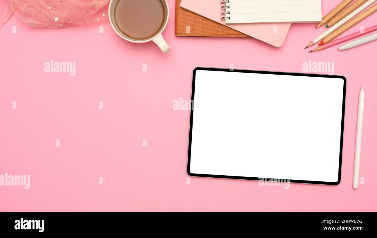 Ein rosa Arbeitsplatz-Hintergrund mit digitalem Tablet-Touchpad, weißem Bildschirm, Stylus-Stift, Teetasse, Schreibwaren und Kopierbereich. Stockfoto