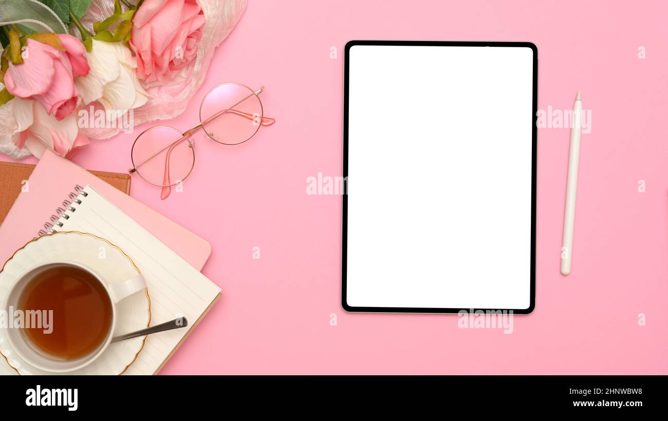 Bürotisch Schreibtisch mit digitalem Tablet-PC mit weißem Bildschirm, Stylus Pen, Brillen, Teetasse, Notizbuch und Rosenstrauß auf rosa Hintergrund. Draufsicht, fl Stockfoto