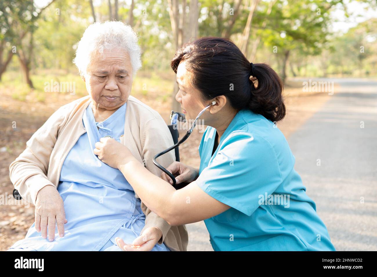 Arzt mit Stethoskop Überprüfung ältere oder ältere alte Dame Frau Patientin, während auf Rollstuhl im Park sitzen, gesund starke medizinische Konzept Stockfoto