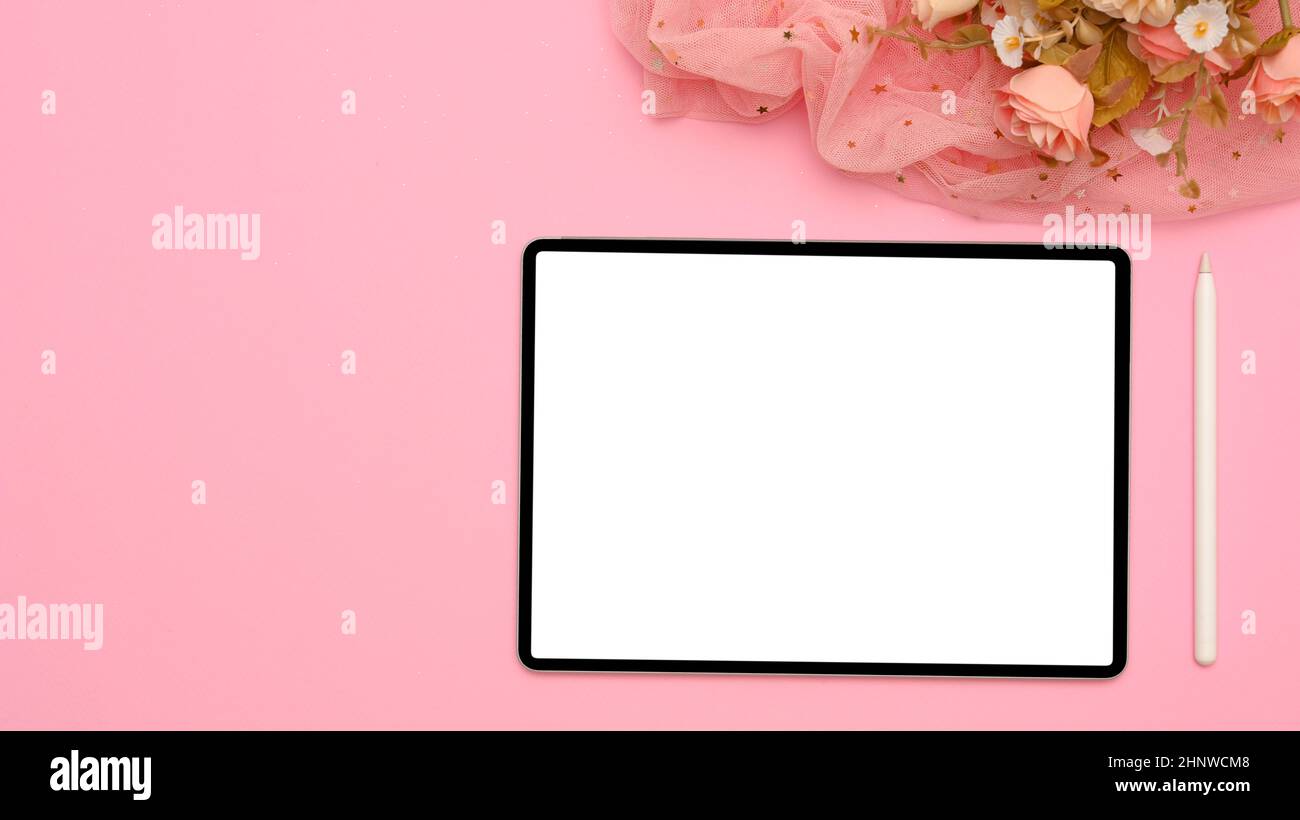 Draufsicht, flaches Lay, weiblicher Arbeitsplatz mit tragbarem Tablet-Computer, weißem Display mit Eingabestift, Blumenstrauß und Kopierraum auf rosa Hintergrund. Stockfoto