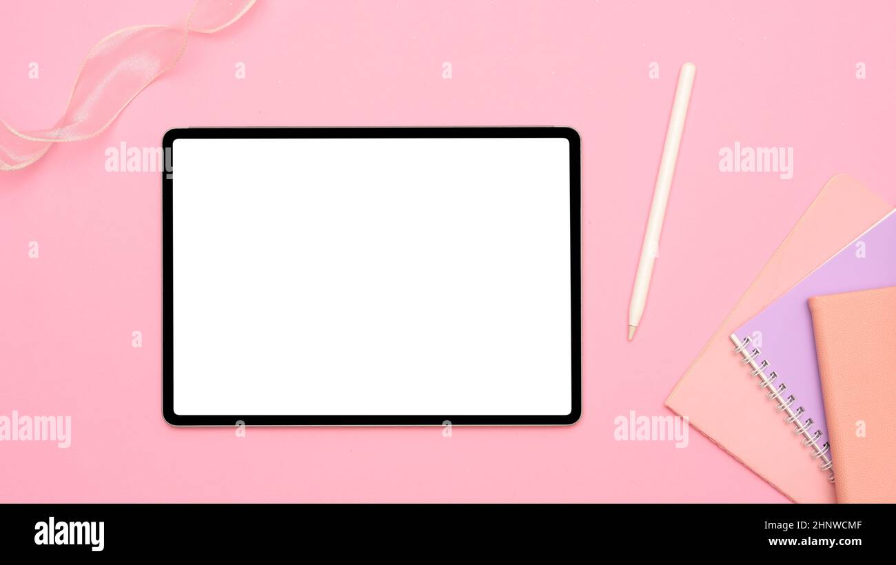 Home Office-Arbeitsplatz mit tragbarem Tablet Touchpad leerem Bildschirm Mockup, Eingabestift und Notebooks auf rosa Tischhintergrund. Oben, flach liegend Stockfoto