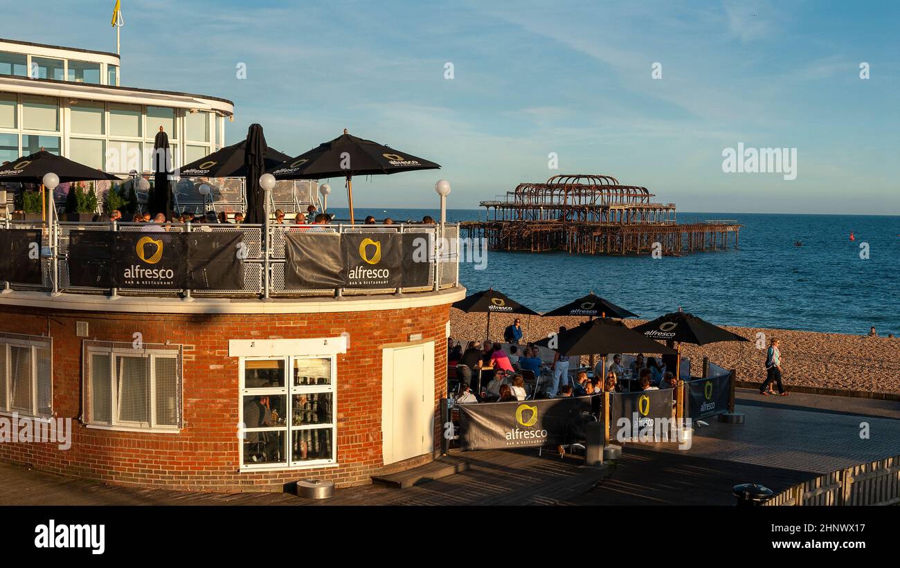 Restaurants und Bars an der Strandpromenade von Brighton mit Blick auf den alten verbrannten West Pier, Brighton, Großbritannien. Stockfoto