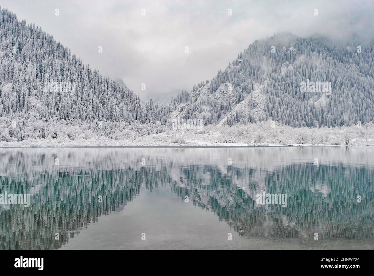 Bergsee im Winter. Schneebedeckte Berge spiegeln sich im Wasser. Winterlandschaft. Stockfoto