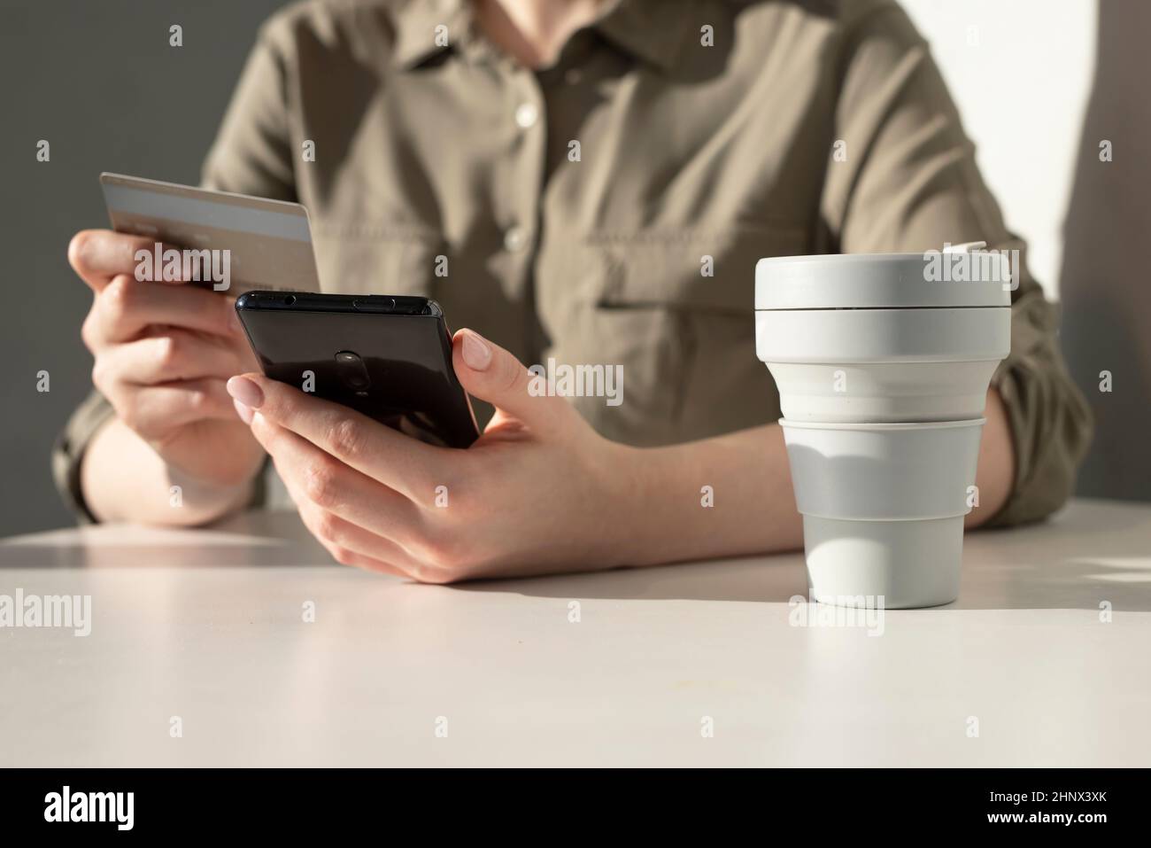 Weibliche Hände mit Kreditkarte und Telefon. Online bezahlen im App-Konzept. Frau sitzt am Tisch mit Take-away-Tasse und online einkaufen. Hochwertige Fotos Stockfoto