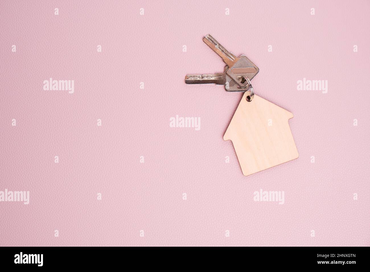 Schlüsselanhänger in Form Haus mit Schlüsseln rosa Hintergrund.Konzept Kauf Haus, Wohnung oder Miete Stockfoto