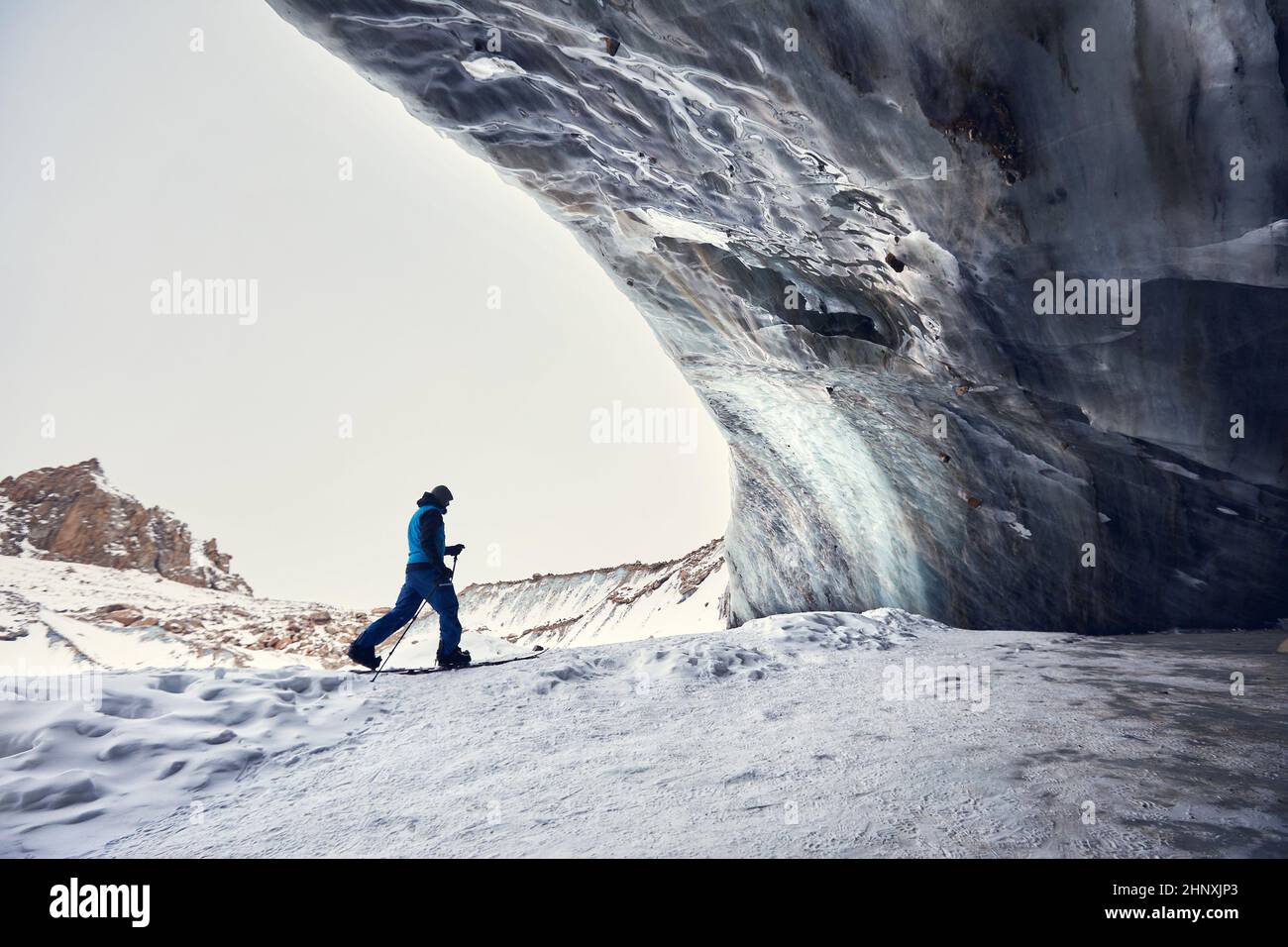 Skifahrer Mann Skitouren in hoch verschneiten Berg Skigebiet Shymbulak in der Nähe von Eishöhlenwand. Sport Outdoor Backcountry Wintersaison. Stockfoto
