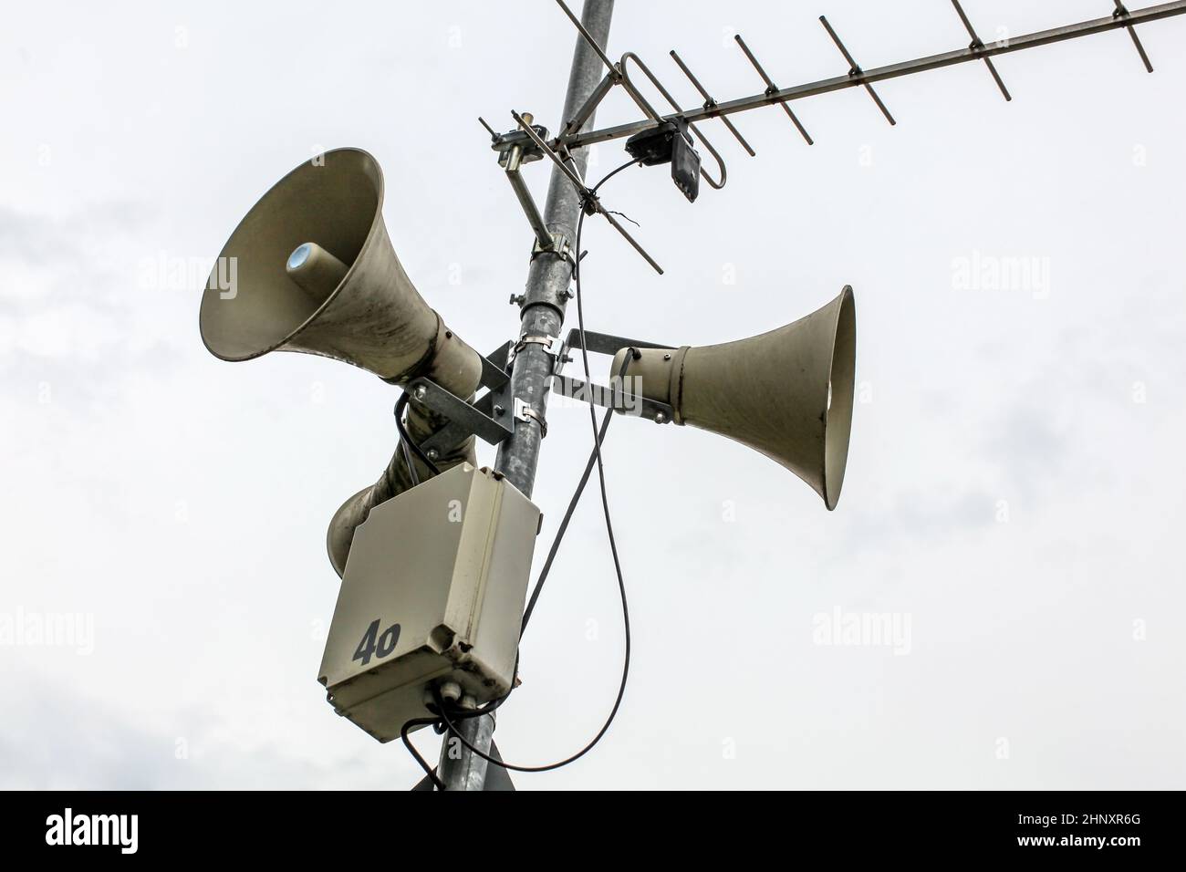 Public Address System Lautsprecher an einer Stange, die Antenne und die Box mit Nummer 46 teilweise abgeblättert, bewölkten Himmel im Hintergrund. Stockfoto