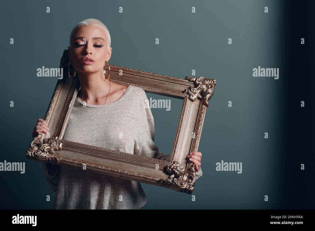 Baguette Framing Workshop Konzept. Junge kaukasische Frau mit kurzen blonden Haaren hält den vergoldeten Bilderrahmen in den Händen Stockfoto