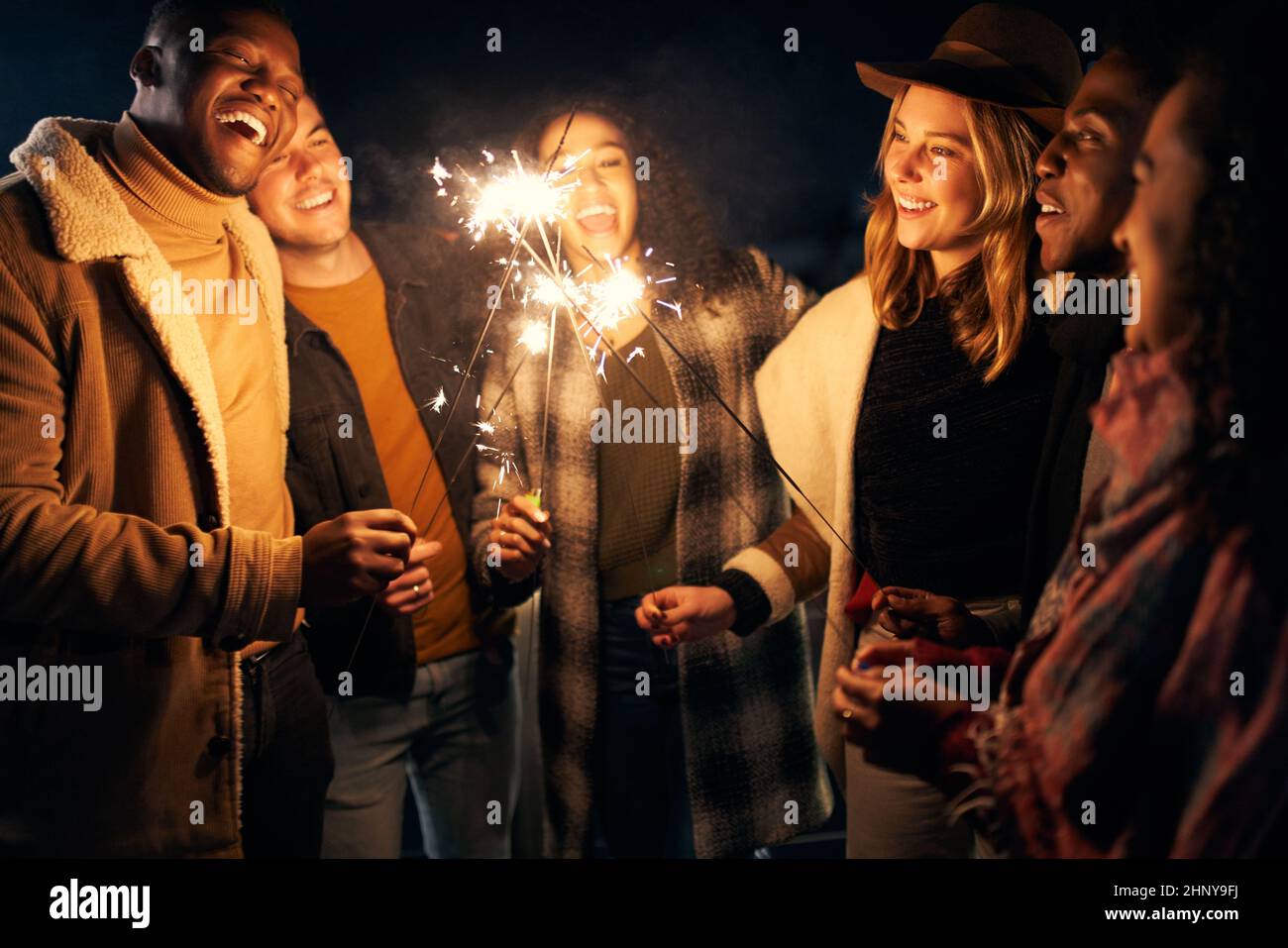 Eine Gruppe von jungen erwachsenen multikulturellen Freunden, die bei einer Dachparty mit Wunderkerzen lachen Stockfoto