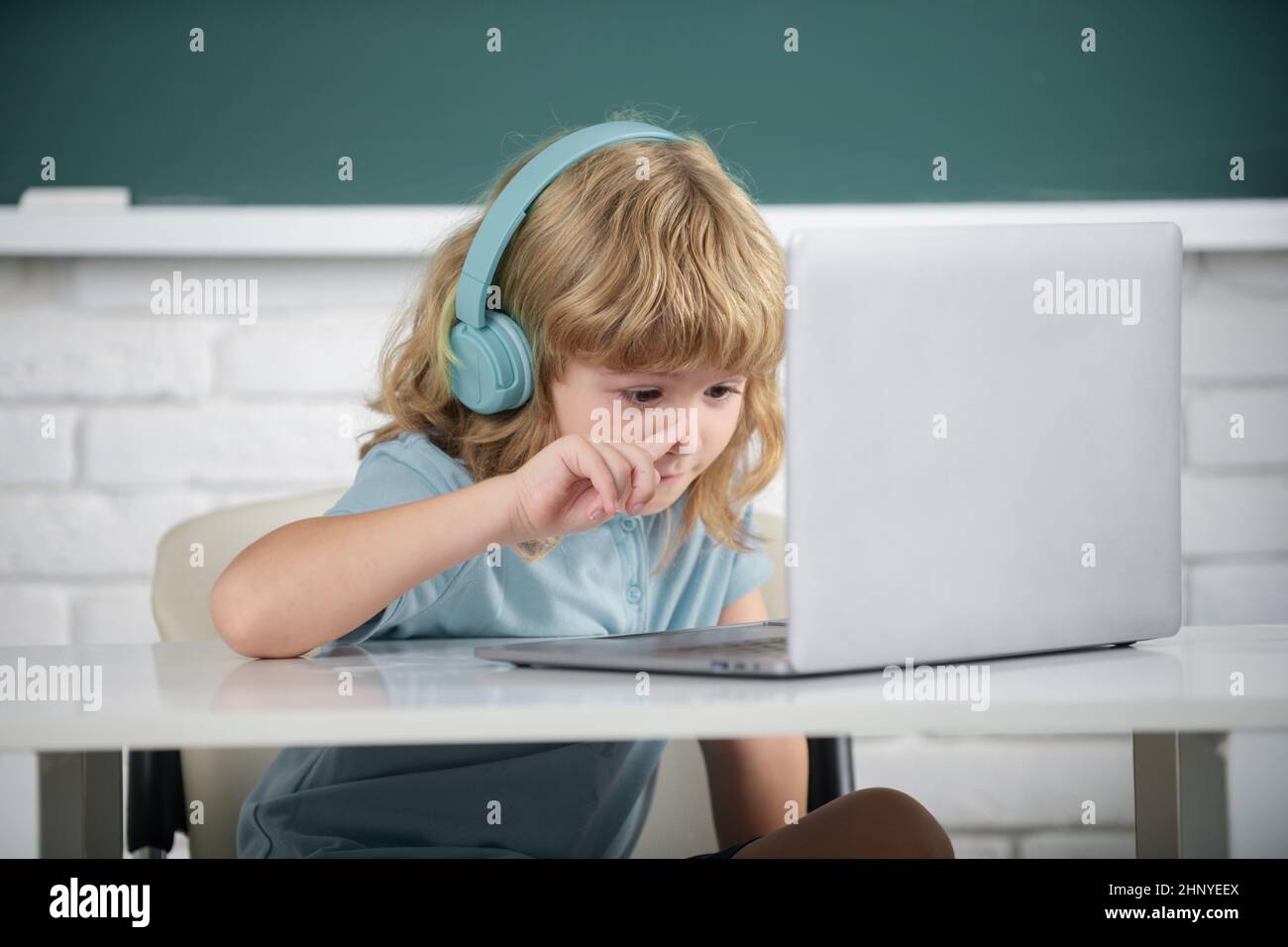 Cleverer Schuljunge, niedlicher Schüler trägt Kopfhörer, die auf dem Laptop schreiben, hören Sie Audiounterricht am Computer. Online-Lerntechnologie. Stockfoto