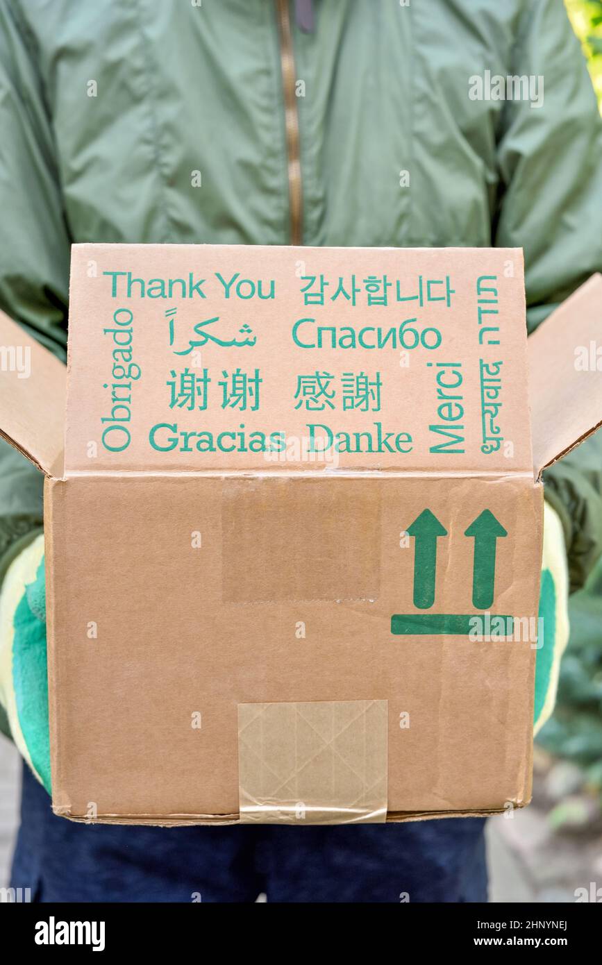 Dankeseinschreibung in verschiedenen Sprachen auf dem Paketkarton in den Händen des Postboten. Stockfoto