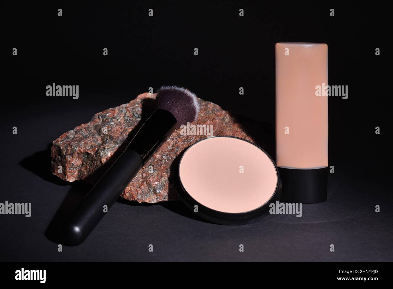 Kosmetikprodukte mit Schminkpinsel und kompaktem Pulver, das auf einem Granitstein auf schwarzem Hintergrund liegt Stockfoto