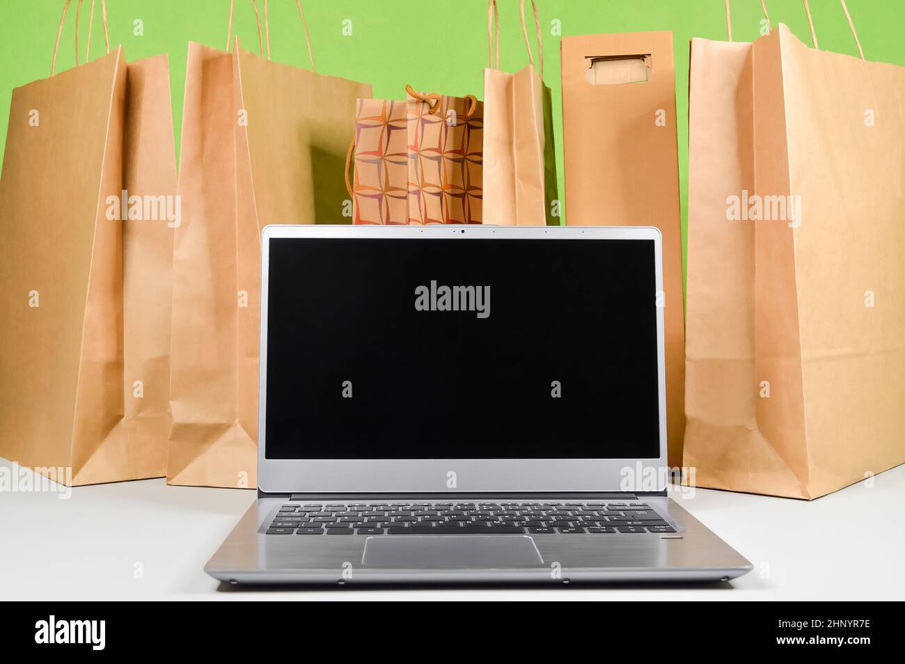 Leerer Bildschirm des Laptop-Computers vor dem Hintergrund von Papiertüten mit Waren und Einkäufen, die auf dem Online-Markt bestellt und nach Hause geliefert wurden Stockfoto