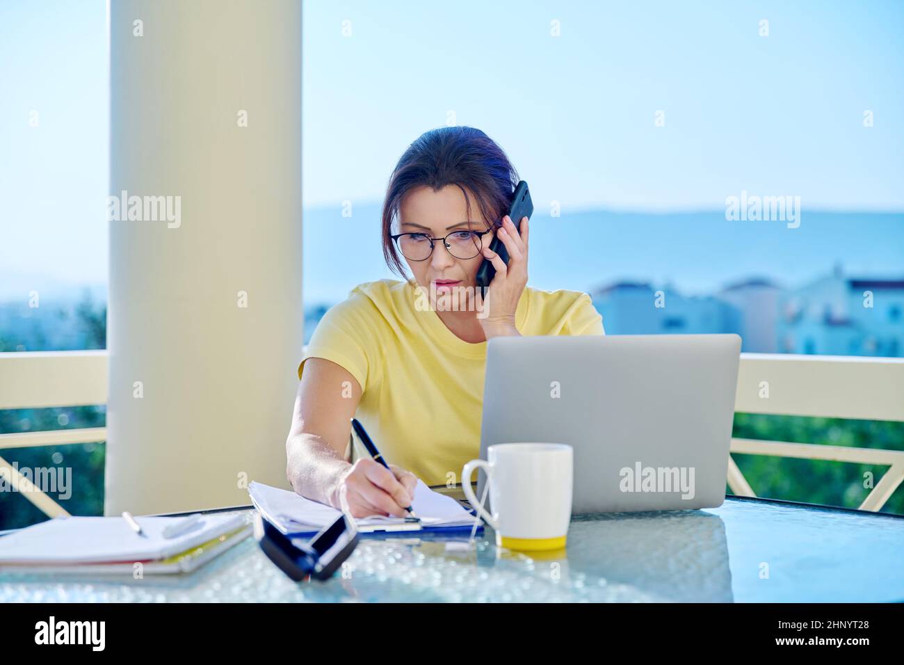 Frau mittleren Alters, die im Heimbüro auf der Terrasse arbeitet und telefoniert Stockfoto