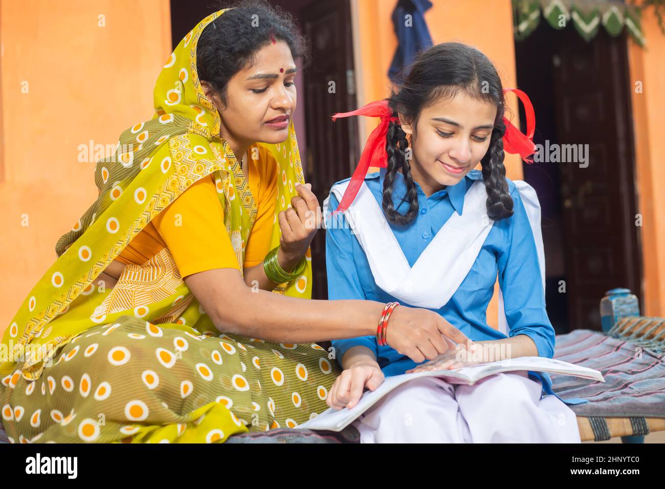 Traditionelle indische Mutter hilft ihrer jungen Tochter in Studien, ländliche Mädchen Kind hält Notebook zu Hause studieren. Stockfoto