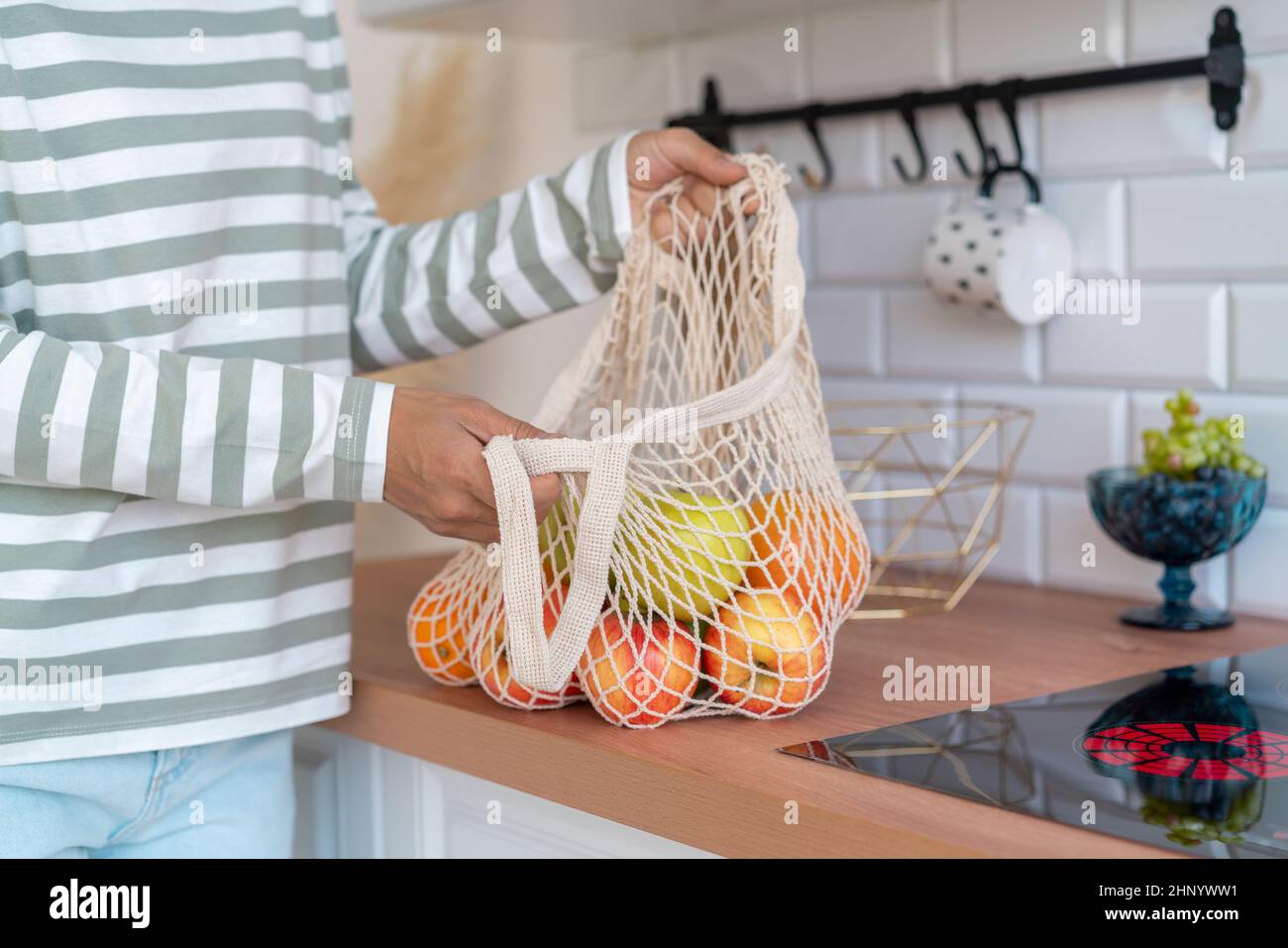 Anonyme Frau, die Lebensmittel in einer Öko-Tasche kauft. Sortieren von Äpfeln in der Küche. Zero Waste Shopping-Konzept Stockfoto