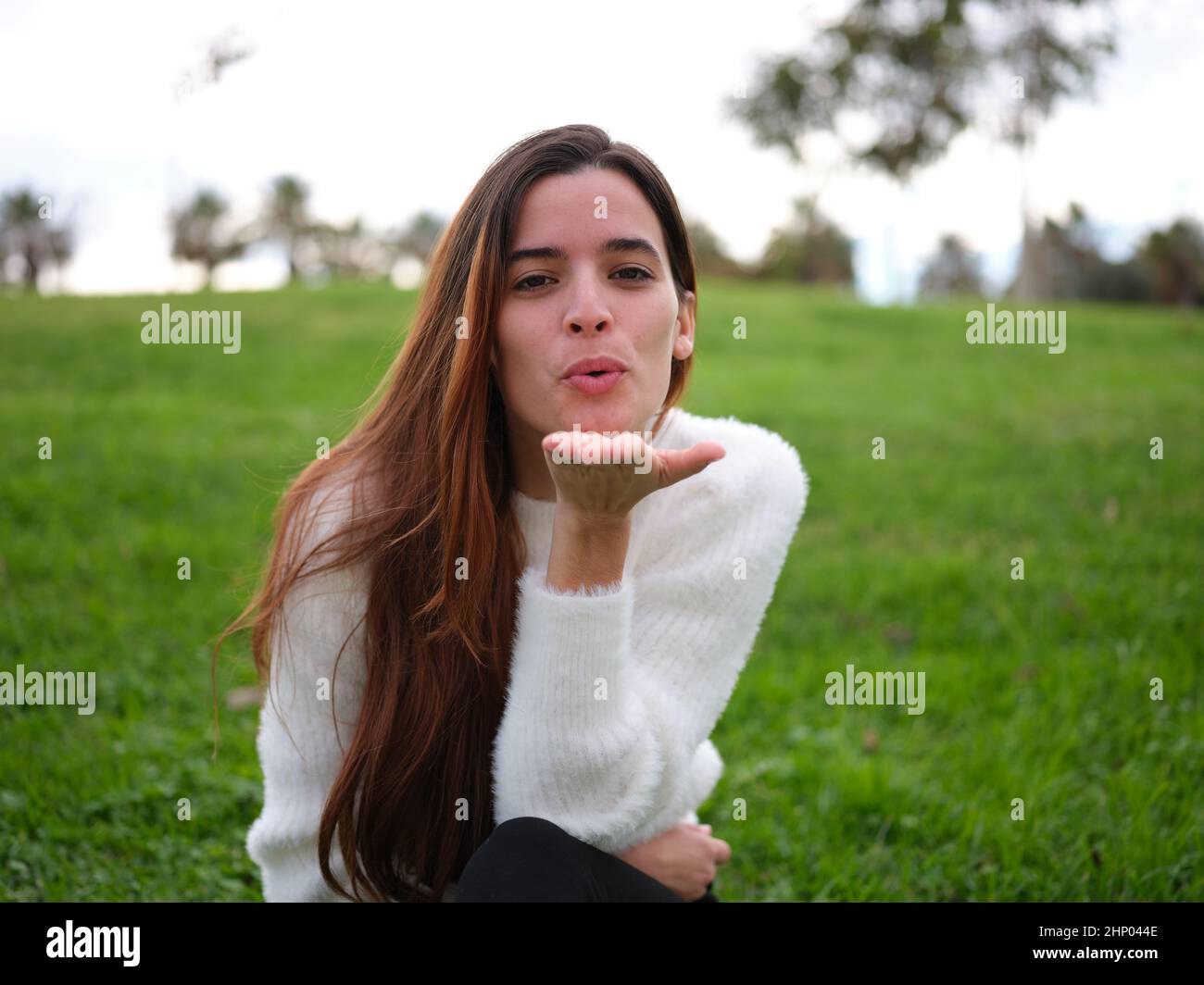 Junges Mädchen in der Liebe im Park bläst einen Kuss auf die Kamera Stockfoto