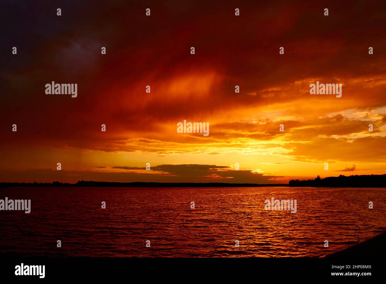 Blutig roter, wolkiger Sonnenuntergang über dem See. Morgen feuriger orangefarbener Sonnenaufgang über dem Fluss. Reflektierende Wasseroberfläche Wellen unter Wolken in der Dämmerung im Sommer. Abend c Stockfoto