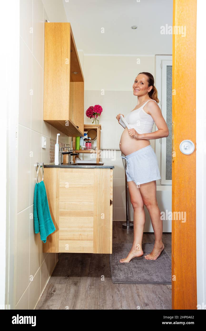 Die Schwangere steht im Badezimmer neben dem Spiegel Stockfoto